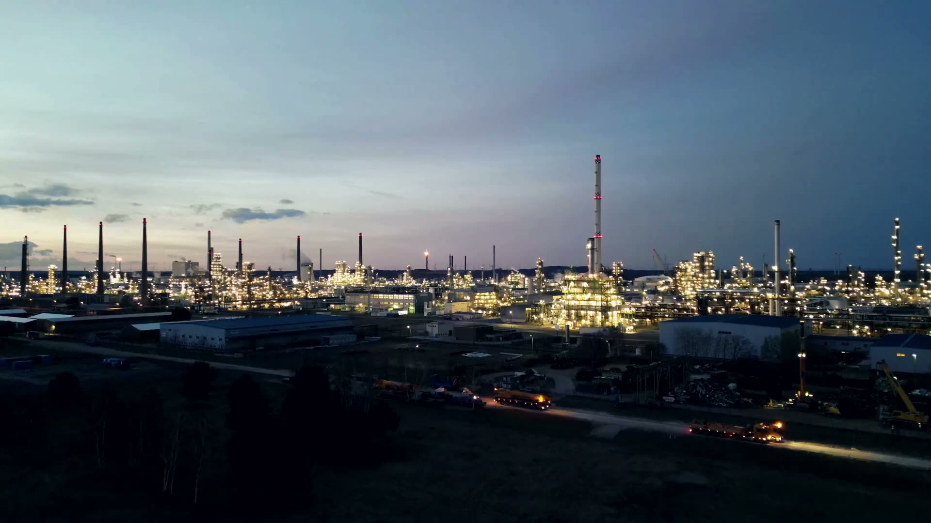 A chemical park at dusk, its towers and flare stacks lit against a blue-hour sky